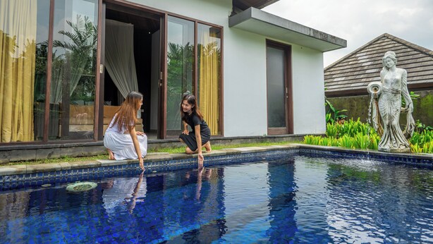 A swimming pool with a statue, a building with large windows, and a person by the pool. - Alpin Resort and Villa Ubud (Ubud)