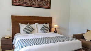 A neatly made bed with a patterned bedspread, a wooden headboard, and a bedside lamp. - Alpin Resort and Villa Ubud (Ubud)