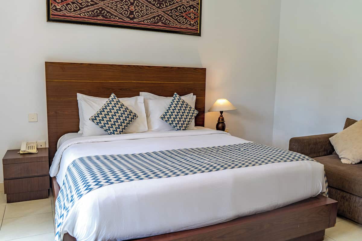 A neatly made bed with a patterned bedspread, a wooden headboard, and a bedside lamp.