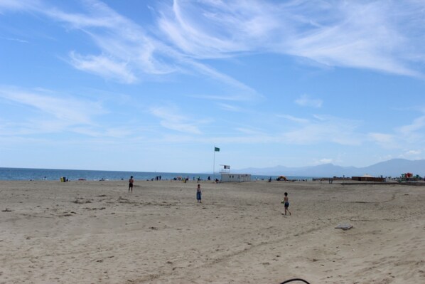 A beach with a flag, people, and a clear sky.