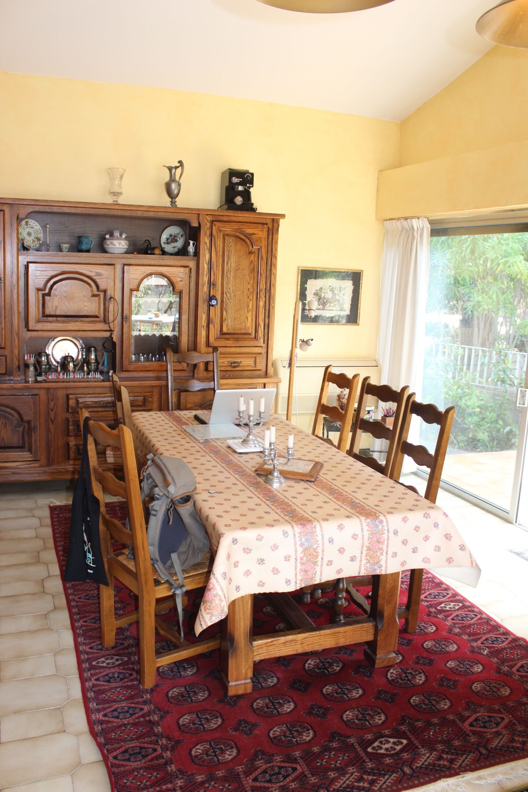 A dining area with a table set for four, wooden chairs, a patterned tablecloth, and a red carpet.