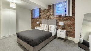 Une chambre avec un grand lit, un mur en briques, deux tables de chevet avec des lampes et une armoire.