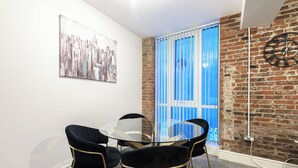 Une pièce avec une table ronde en verre, quatre chaises noires, une horloge au mur et un rideau bleu.