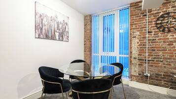 A room with a round glass table, four black chairs, a clock on the wall, and a blue curtain.