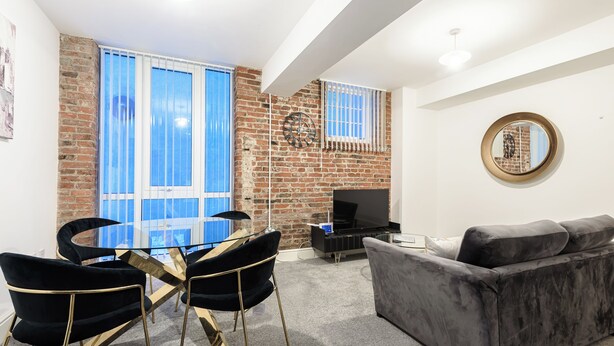 Un salon avec un mur en briques, un canapé, un téléviseur et une table à manger avec des chaises.