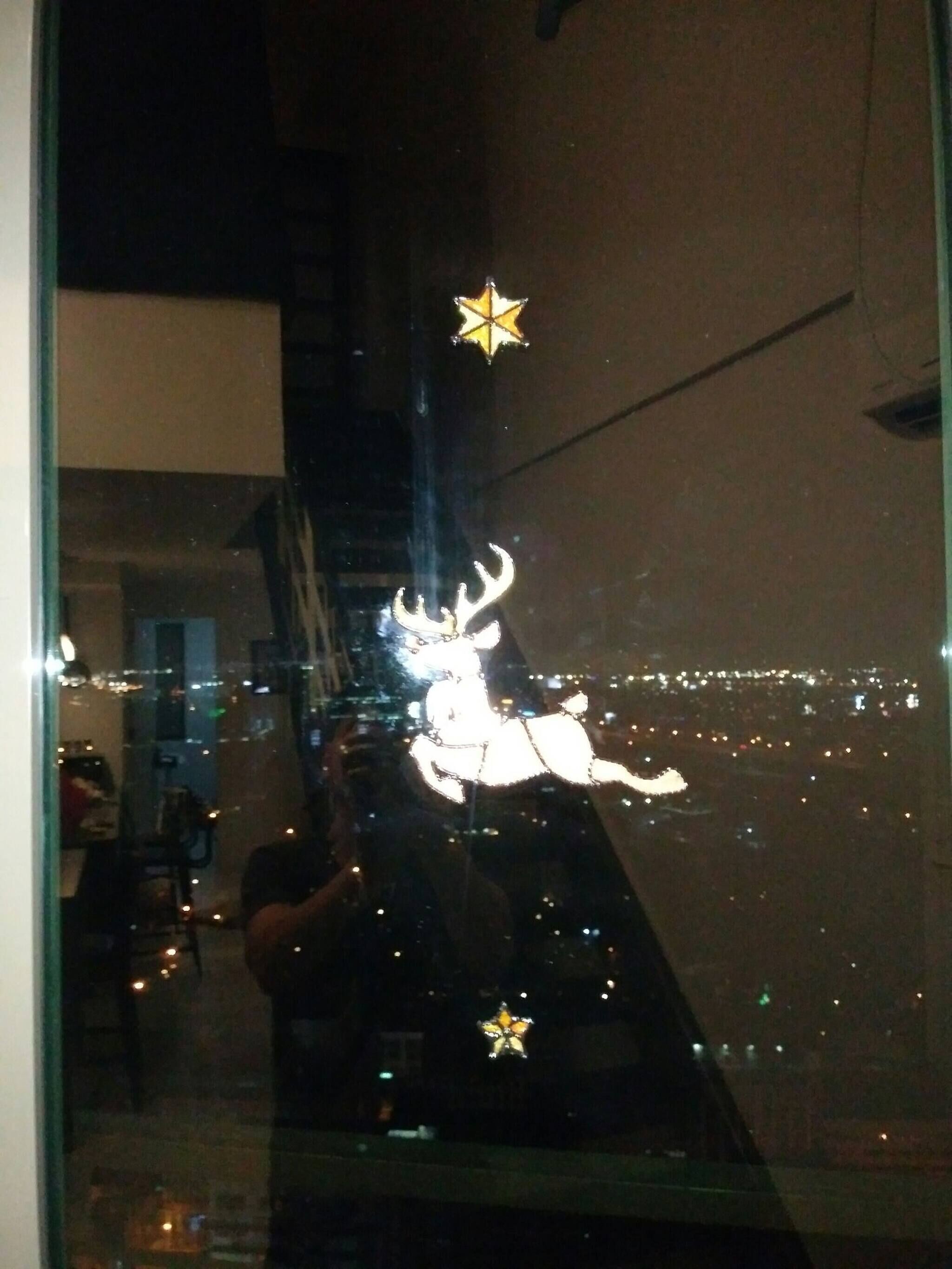 A reflection of a building with a large, illuminated deer figure on a window.