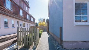 A narrow alleyway with a wooden fence, a paved path, and buildings on either side. - Fitters' accommodation Kuddel (Laboe)