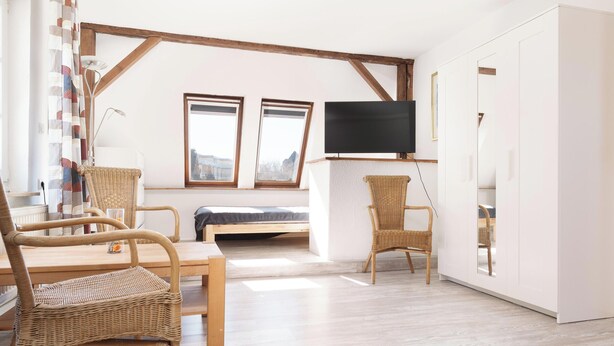 A room with a bed, a TV, wicker furniture, and a window. - Fitters' accommodation Kuddel (Laboe)