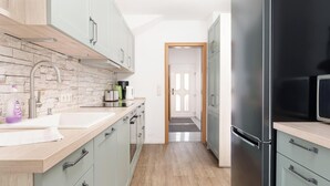 A modern kitchen with light green cabinets, a stainless steel refrigerator, and a stone backsplash. - Fitters' accommodation Kuddel (Laboe)
