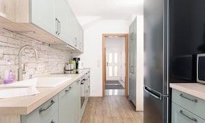 Une cuisine moderne avec des meubles de couleur vert clair, un réfrigérateur en acier inoxydable et un pare-feu en pierre.