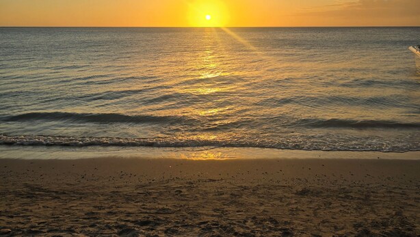 Uma praia com pôr do sol, ondas e areia.