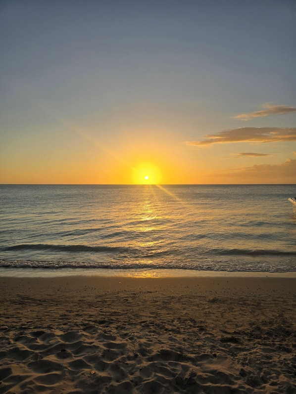 Una playa con atardecer, olas y arena.