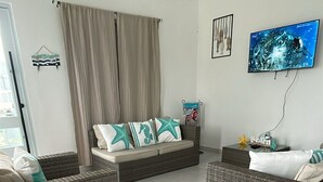 A living room with a ceiling fan, a television mounted on the wall, a sofa with cushions, and a wicker chair. - Casa Cielomar, private pool, BBQ, Billiards, 12 people, pets allowed, Combate Beach (El Combate)
