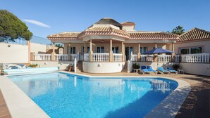 Una piscina con zona cubierta, sillas de descanso y una valla.