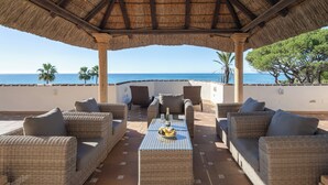 Un área de estar al aire libre con muebles de mimbre, una mesa con una botella y vasos, y vista al mar.