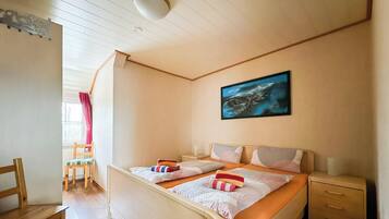 Ein Schlafzimmer mit zwei Betten, einem Fenster mit Vorhängen, einem Nachttisch und einem Bild an der Wand.