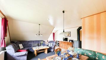 Ein gemütlicher Wohnbereich mit Sofa, Esstisch für zwei Personen, Fernseher und Kamin.