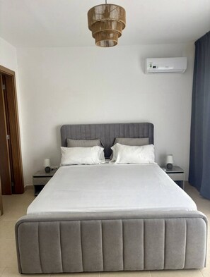A bedroom with a large bed, two bedside tables, a wall-mounted air conditioner, and a hanging light fixture. - Casa Tortuga Sal Apartment 1st Floor With Balcony (Sal)