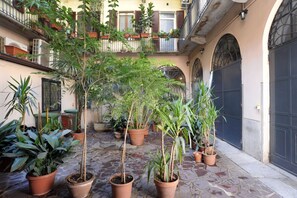 Ein Innenhof mit Blumentöpfen, gefliestem Boden und einem Gebäude mit Balkonen und einer dunklen Tür.