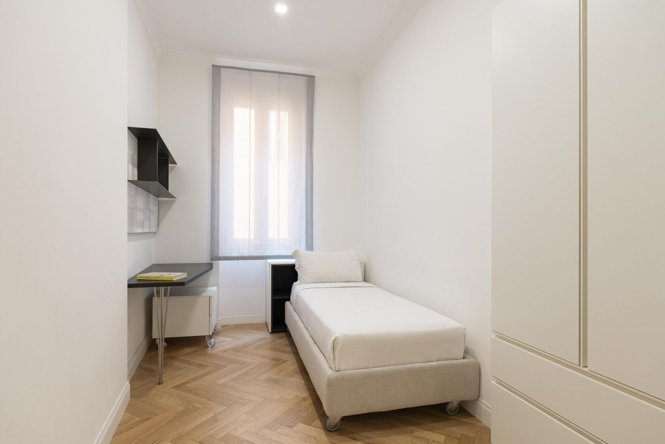 A small, compact room with a bed, a desk, and a chair.