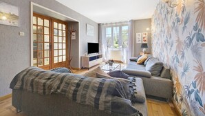 A living room with a sofa, a television, a coffee table, and a window with curtains.
