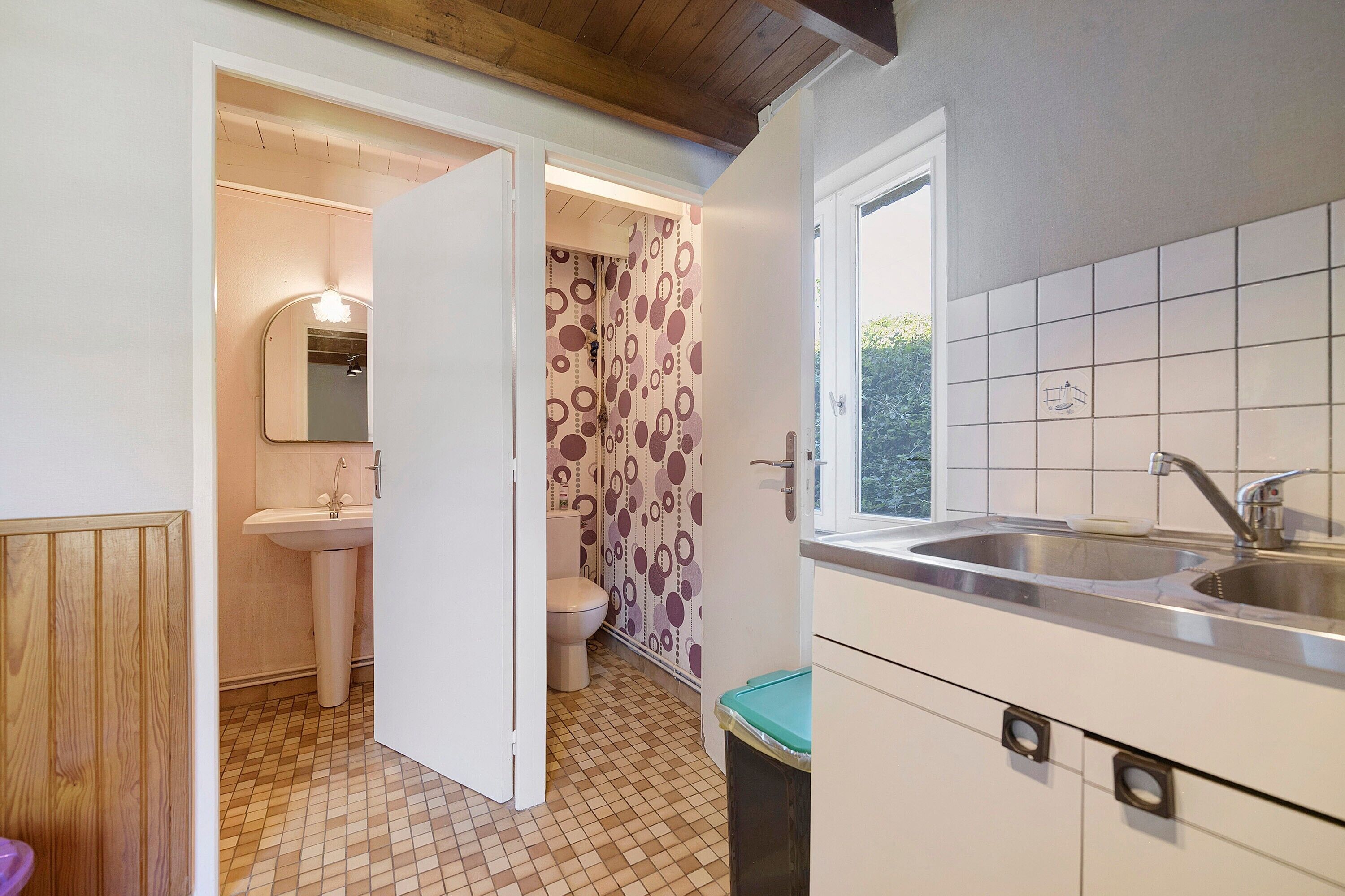 A bathroom with a toilet, sink, and mirror; a kitchen with a sink and window; and a tiled floor.
