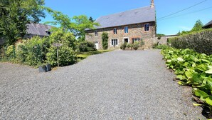 A stone building with a gravel driveway, a sign reading 'GITE,' and lush greenery.