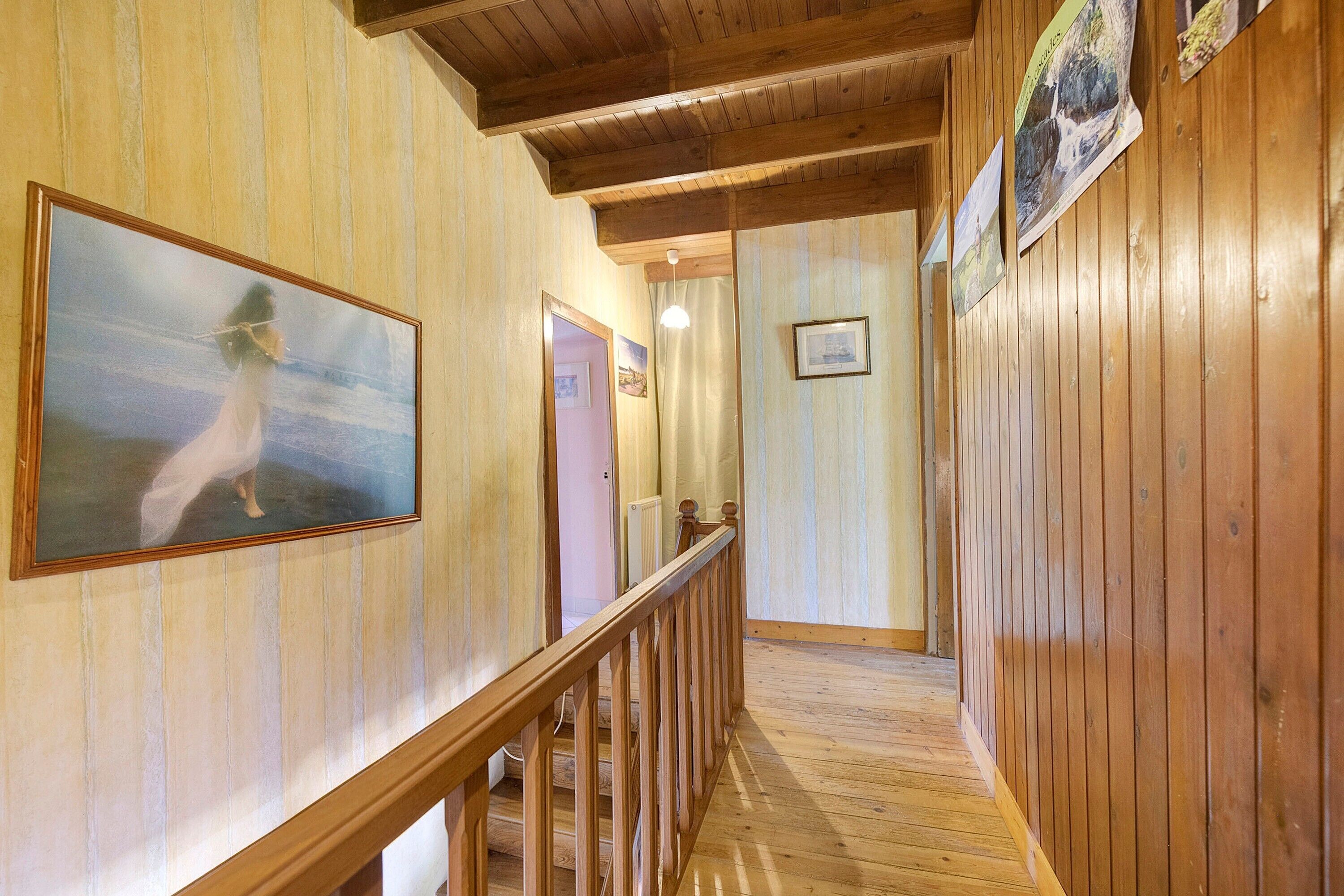 A wooden interior hallway with a staircase, wooden walls, and framed pictures.