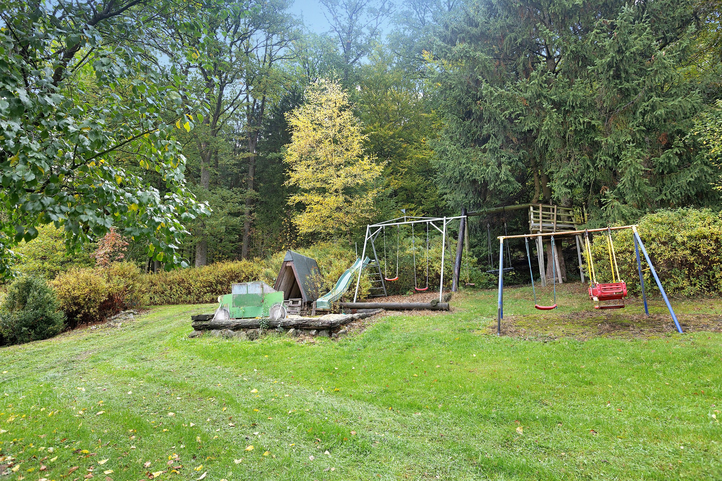 A playground with swings and a slide, surrounded by trees and grass.