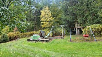 A playground with swings and a slide, surrounded by trees and grass.
