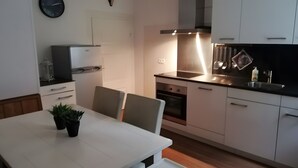 Ett modernt kök med vita skåp, ett matbord med stolar, en inbyggd ugn och en klocka på väggen.