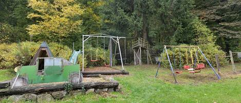 Un parque infantil con columpios y un tobogán, rodeado de árboles y césped.