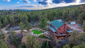 A large, multi-story cabin with a green roof, surrounded by dense forest, and a small lawn with outdoor seating. - Mountain Home on 8 Acres - Amazing Views / Outdoor Spaces - 19 Min to DGO (Durango)