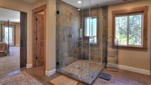 A modern bathroom with a glass-enclosed shower, a wooden door, a window with a view of trees, and a stone-tiled floor. - Mountain Home on 8 Acres - Amazing Views / Outdoor Spaces - 19 Min to DGO (Durango)