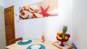 Un coin repas avec une table en bois, deux chaises, un panier de fruits, une bouteille et un verre à vin.