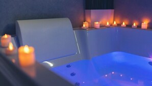 Un espacio de spa con una bañera, múltiples velas y una pared oscura.