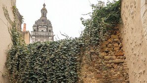 Un estrecho callejón con un muro de piedra, una puerta de madera y vistas a un edificio distante con una torre.