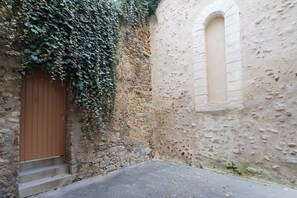 Une ruelle étroite, avec un mur de pierre, une porte en bois et une fenêtre.