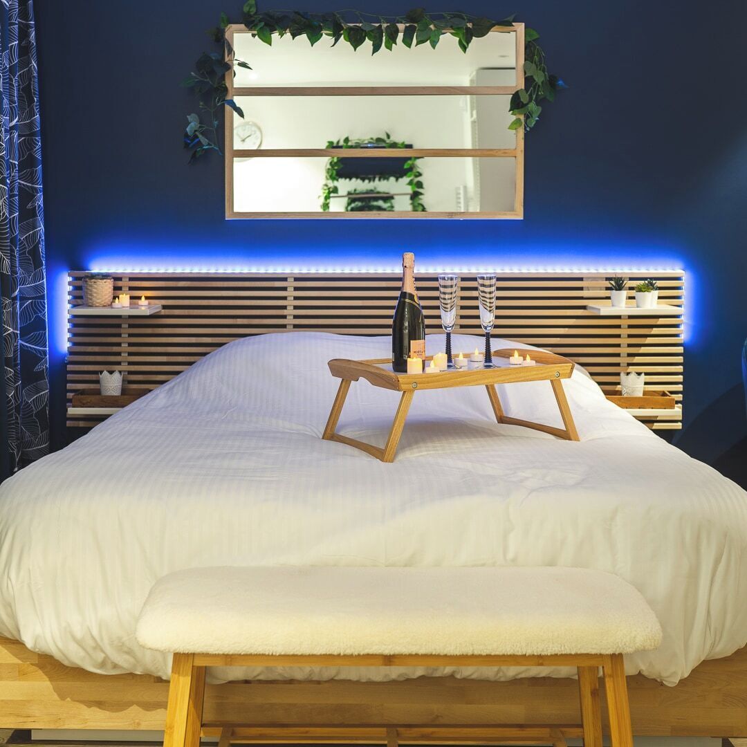 Een bed met een houten hoofdbord, een nachtkastje met een fles en glazen, en een spiegel erboven.