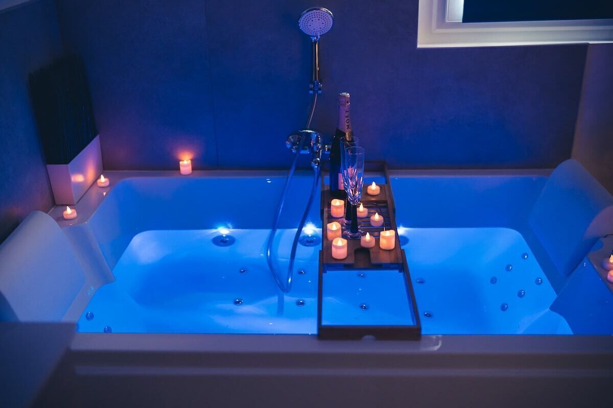 Een badkuip met kaarsen en een fles, waarschijnlijk voor aromatherapie of ontspanning.