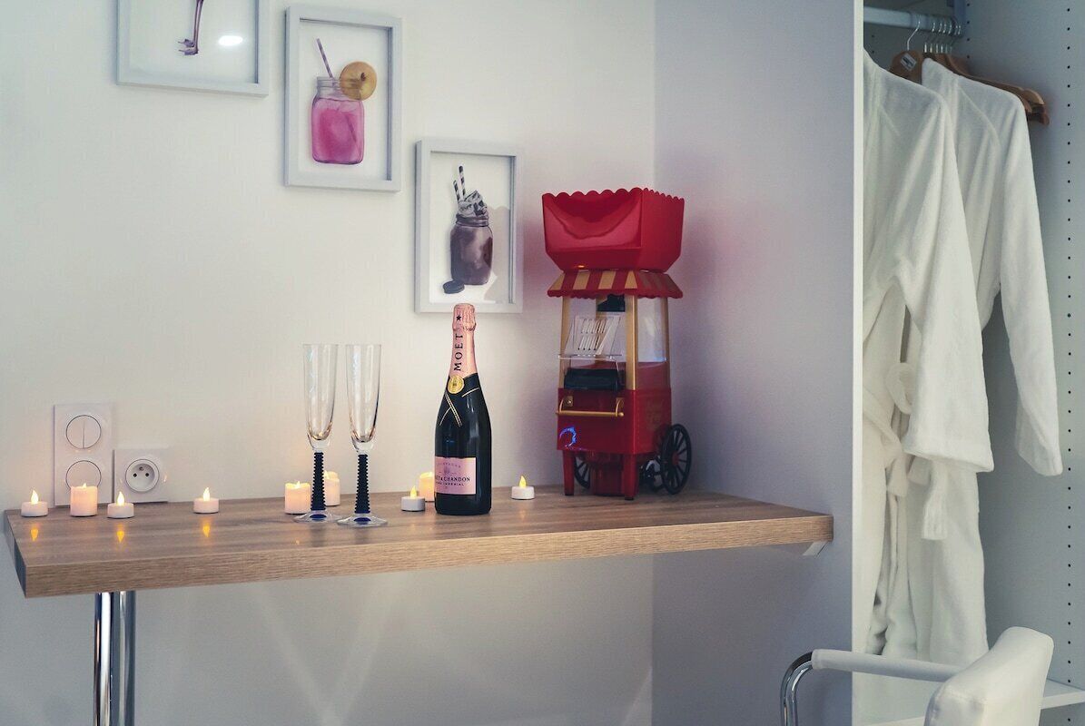 Een kamer met een houten plank waarop champagne, kaarsen en een lijst met kunstwerken staan.