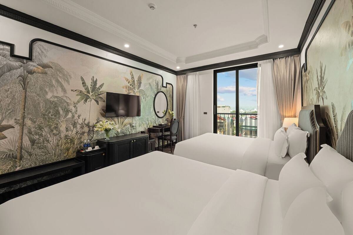Ein Hotelzimmer mit einem großen Bett, einem Schreibtisch mit Stuhl, einem Fernseher und einem Balkon mit Vorhängen.
