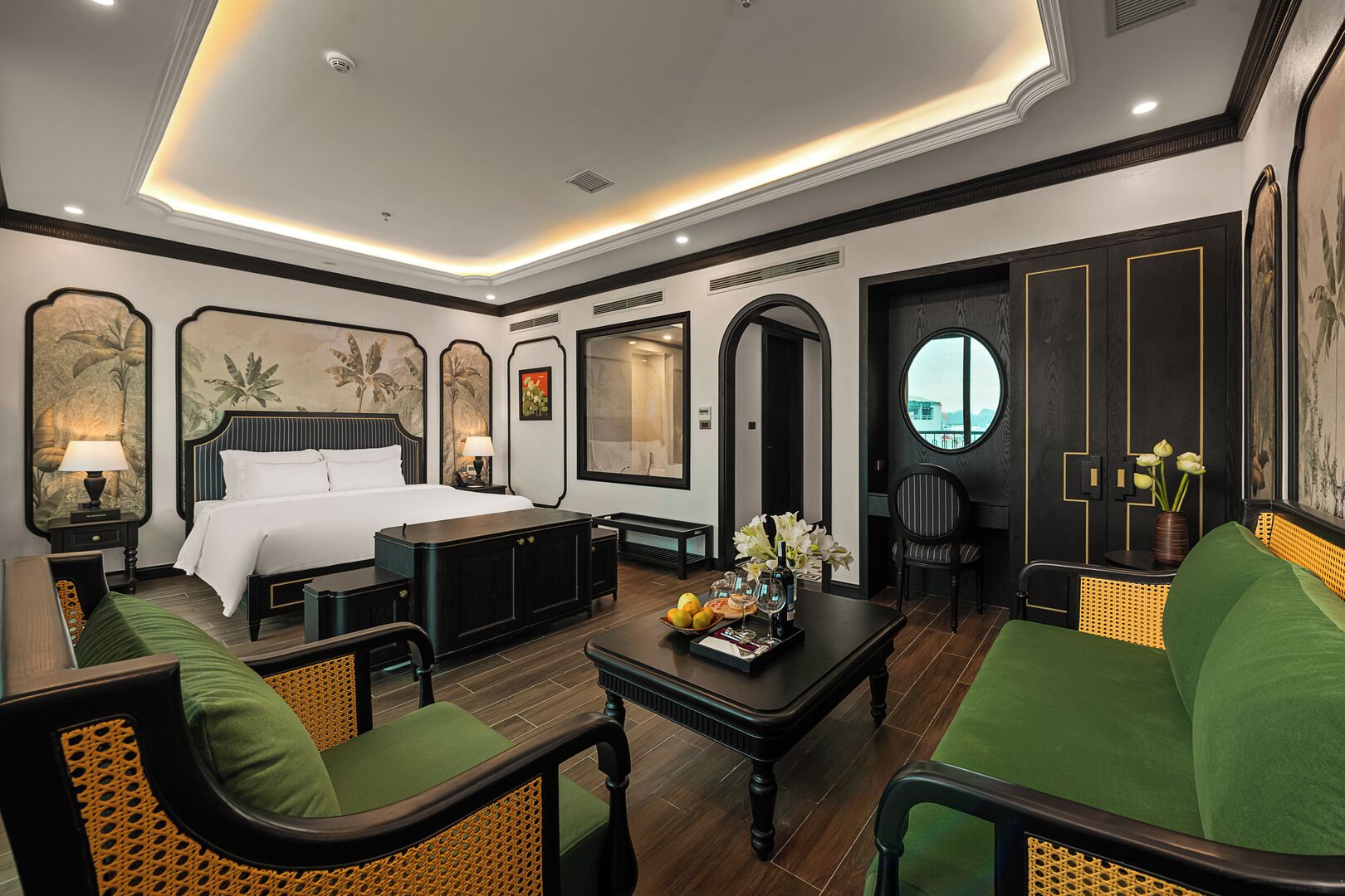 A hotel room with a bed, a sofa, a dining table, and a chair. There is a window with a view.