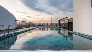 En pool på taket med fri utsikt över stadens silhuett, en modern arkitektonisk design och en glasvägg.