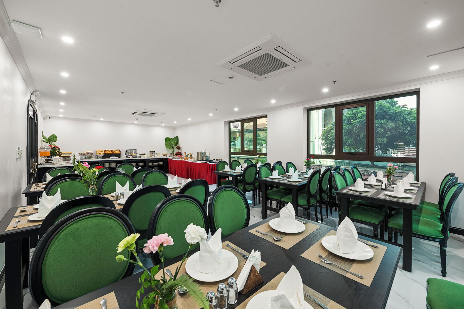 A dining area with green upholstered chairs, white table settings, and a buffet in the background.