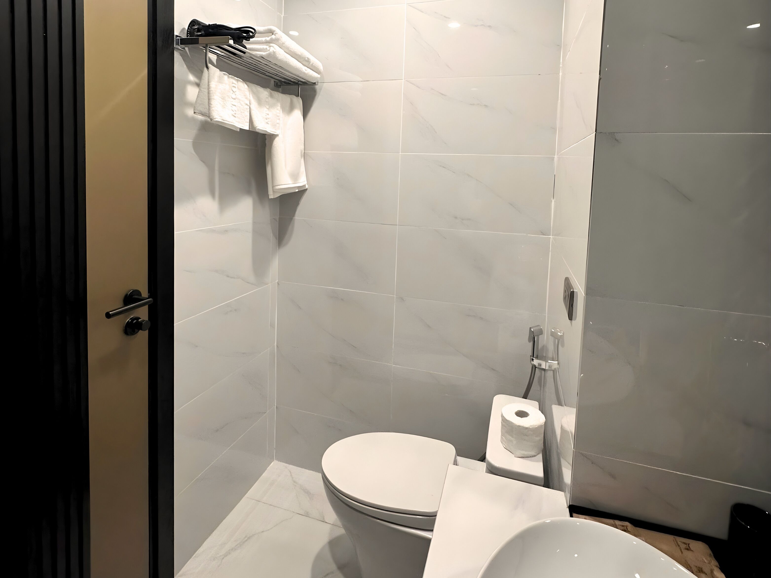 A modern bathroom with a toilet, a towel rack with folded towels, a toilet paper holder, and a shower area.