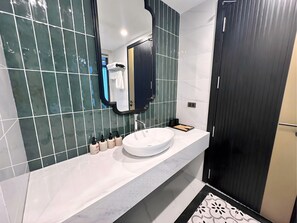 Une salle de bain moderne avec un lavabo blanc, des carreaux vert foncé, un grand miroir et une porte noire.