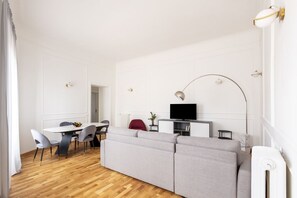 A modern living room with a sofa, dining table, chairs, a TV, and a lamp. - This beautiful apartment is located at Largo di Pietro Brazza 26, on the fourth floor. It is very bright and features two bedrooms, one of which has an en-suite bathroom. The spacious living room, an additional bathroom, and a fully equipped kitchen with (Roma)