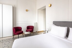 A hotel room with a large bed, two red armchairs, a small table, and a radiator. - This beautiful apartment is located at Largo di Pietro Brazza 26, on the fourth floor. It is very bright and features two bedrooms, one of which has an en-suite bathroom. The spacious living room, an additional bathroom, and a fully equipped kitchen with (Roma)