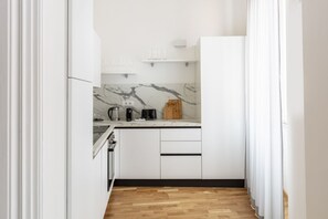 A modern kitchen with white cabinets, a marble backsplash, and a wooden floor. - This beautiful apartment is located at Largo di Pietro Brazza 26, on the fourth floor. It is very bright and features two bedrooms, one of which has an en-suite bathroom. The spacious living room, an additional bathroom, and a fully equipped kitchen with (Roma)